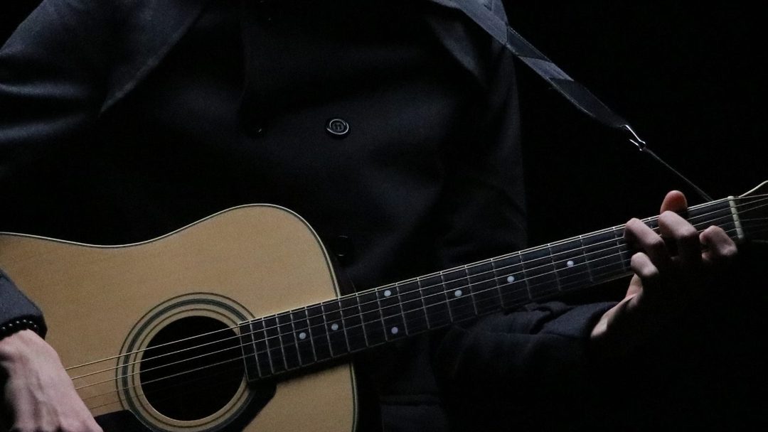 Mão posicionada no braço do violão em close, mostrando a técnica de dedos sobre as cordas.