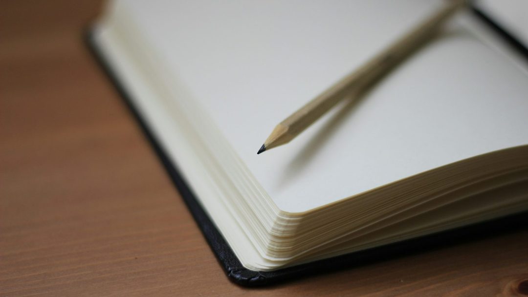 Caderno fechado com um lápis apoiado sobre uma mesa de madeira.