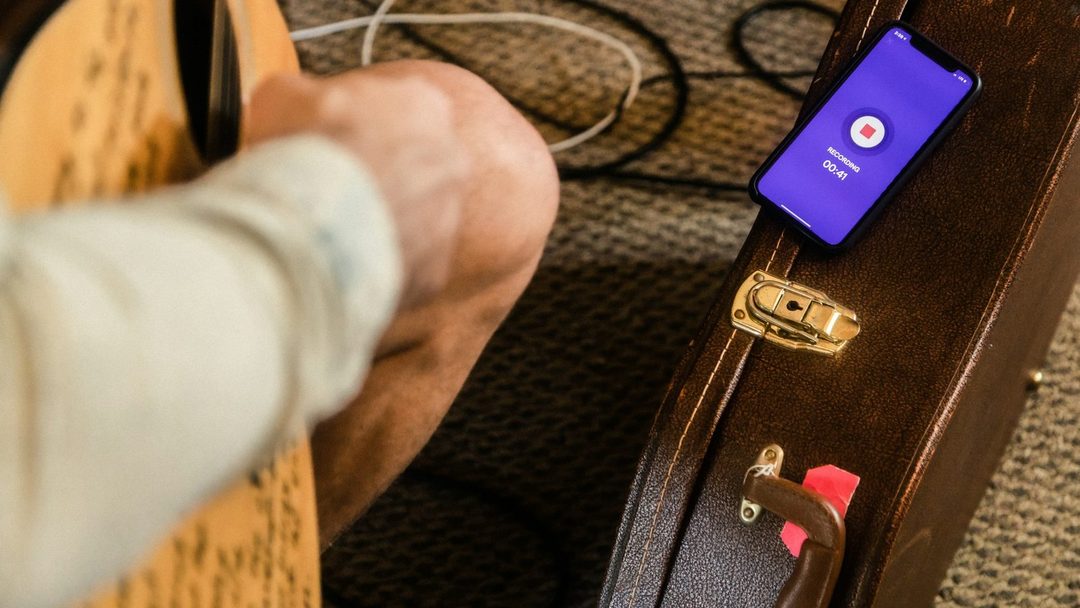 Mão próxima ao estojo do violão, com um celular mostrando um aplicativo de estudo.