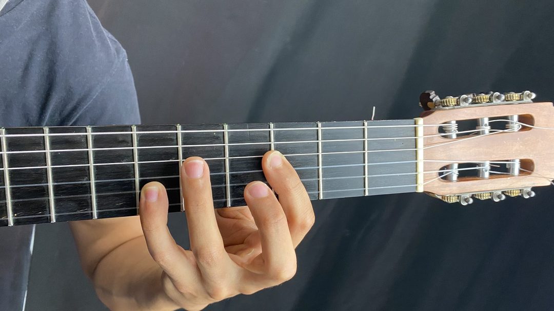 Close da mão esquerda fazendo pestana no braço de um violão clássico de cordas de nylon
