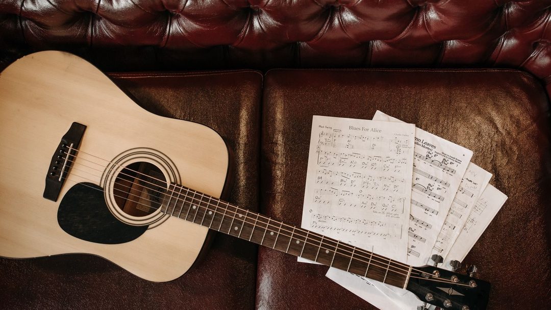 Violão acústico deitado ao lado de folhas de partitura manuscrita sobre um sofá de couro