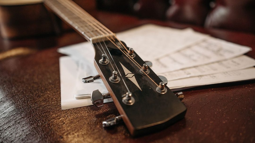 Braço e cordas de um violão apoiado sobre folhas de partitura em um sofá de couro