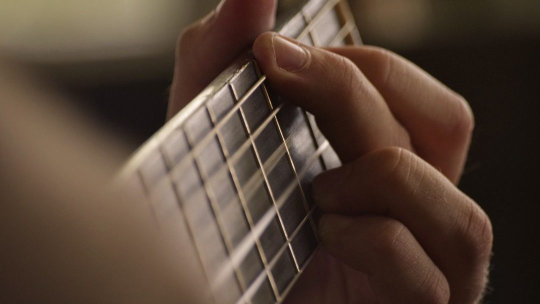 Mão formando um acorde no braço do violão, com boa iluminação.