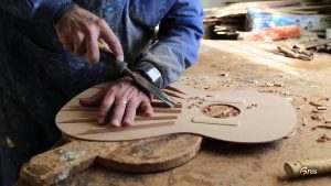 Luthier trabalha a madeira do tampo de um violão em construção