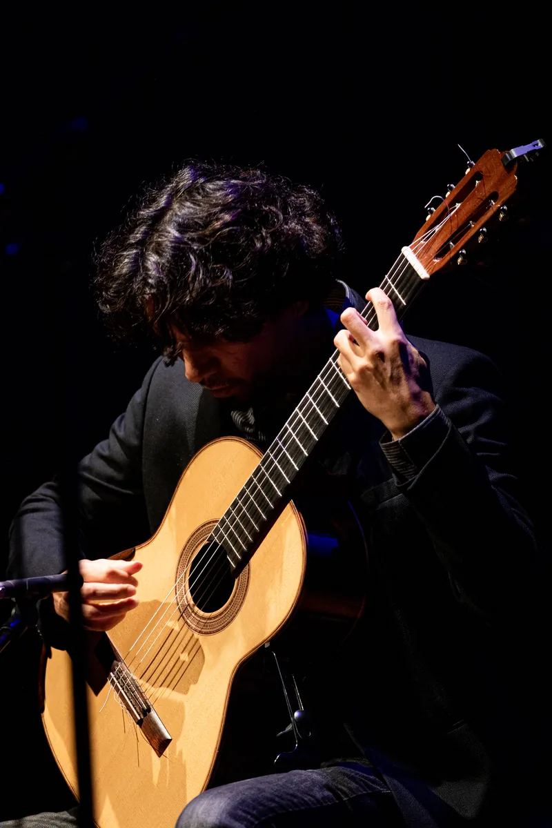 Luis Leite em concerto, violão sob luz quente em palco escuro